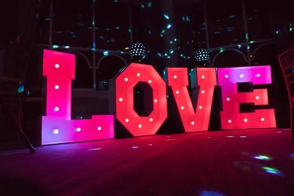 Freestanding LOVE letters illuminated in pink beneath coloured party lighting
