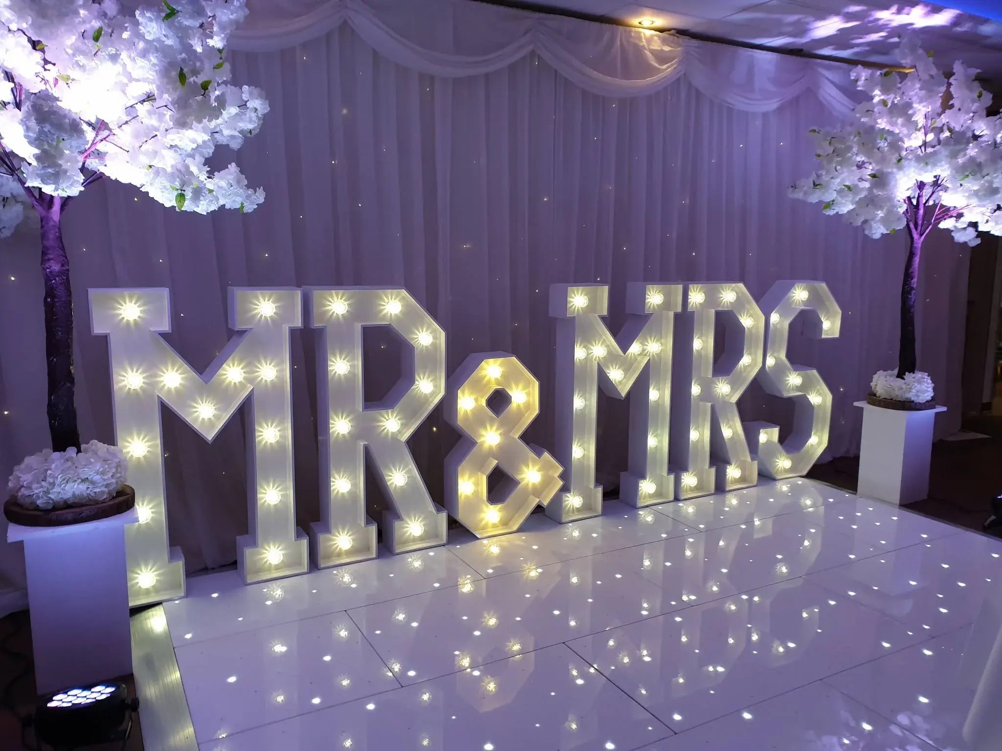 White illuminated MR & MRS letters beside floral trees and a star-lit dance floor