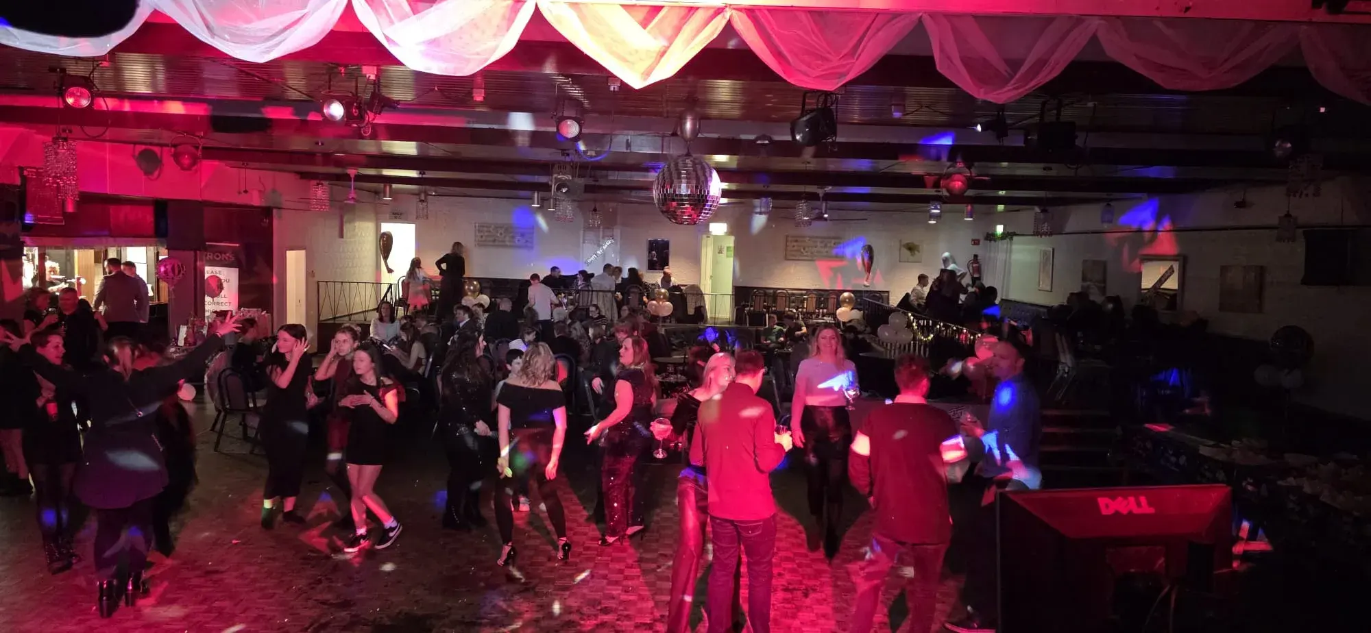 Party guests dancing in a function room beneath a mirror ball and red lighting
