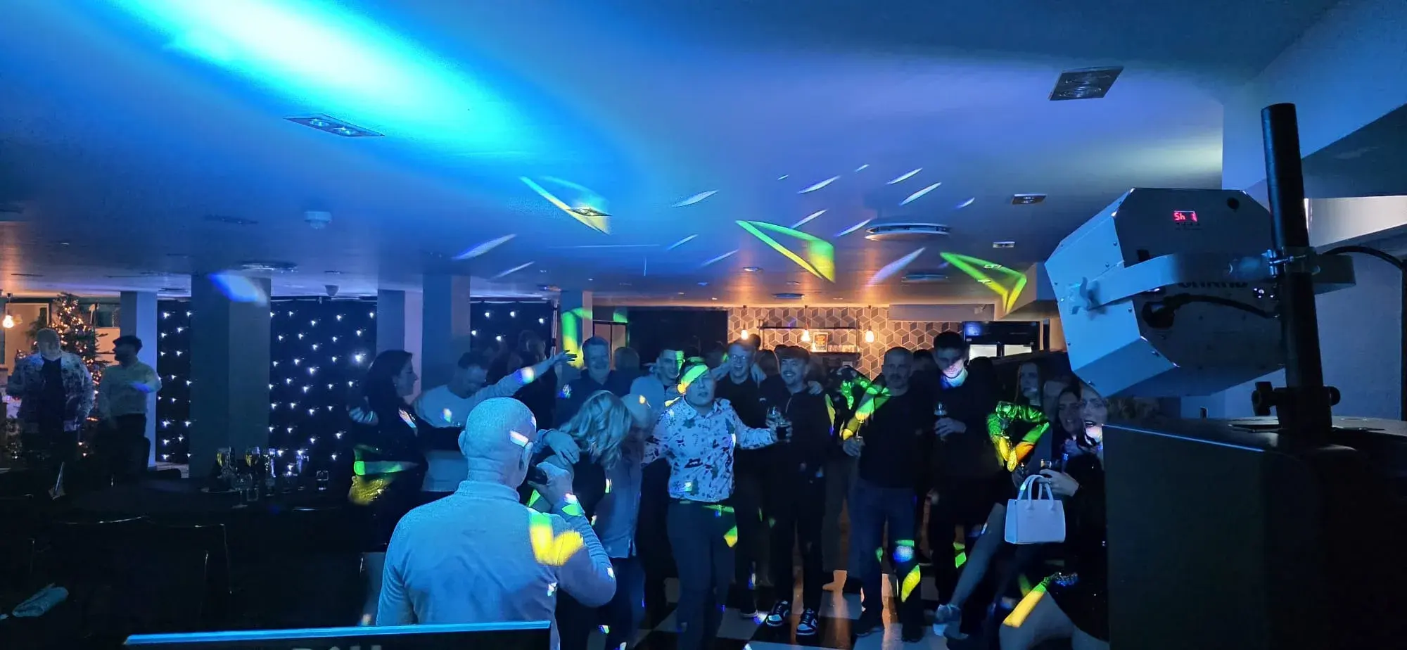A guest holding a microphone in front of a group of party guests under blue lighting