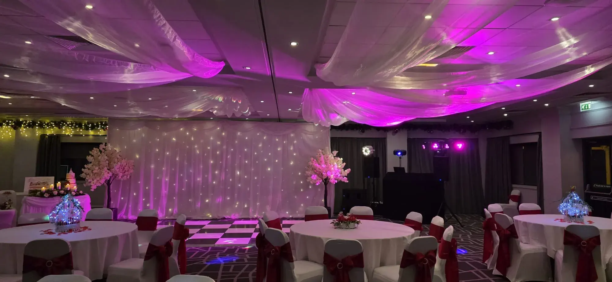 A reception room with pink lighting, a fairy-light backdrop and a checkerboard dance floor