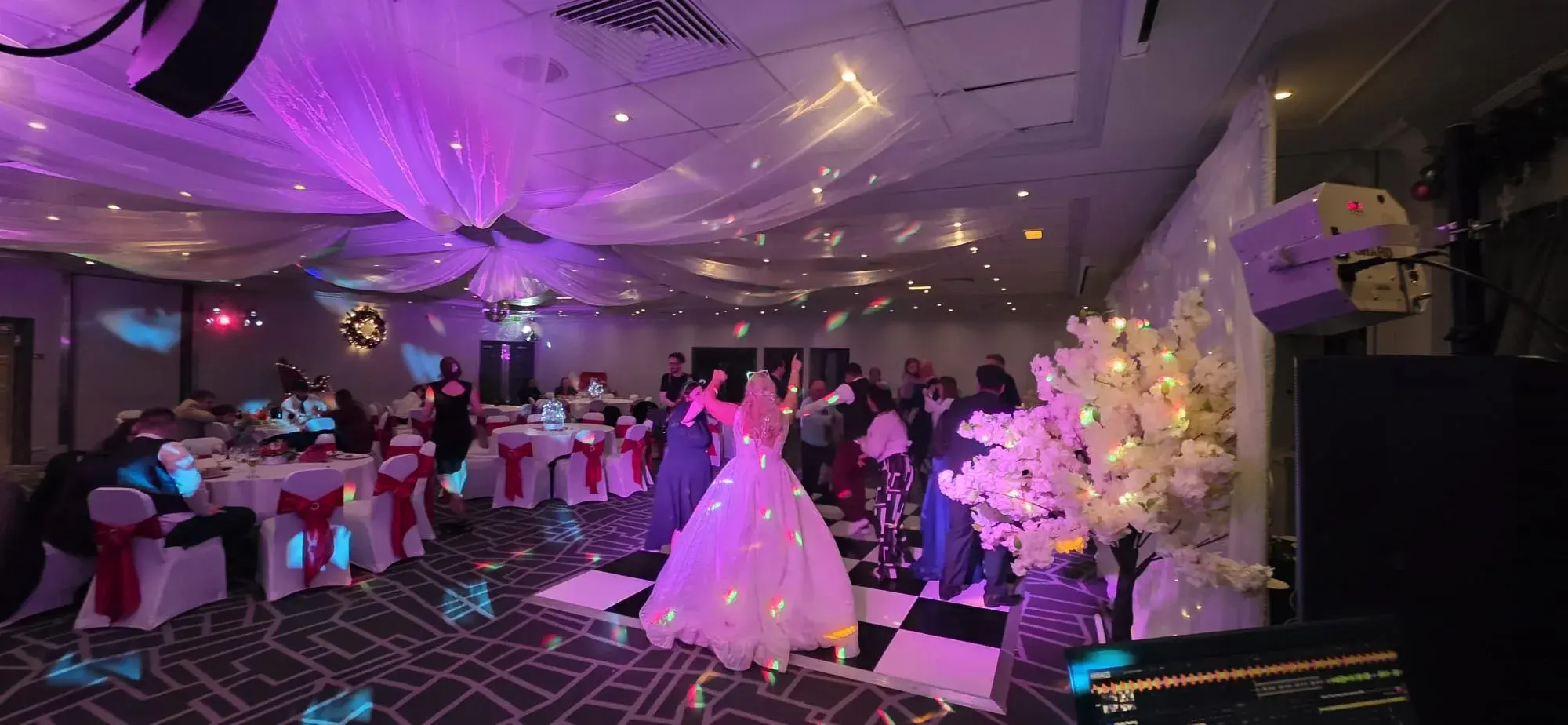 A bride dancing on a checkerboard floor with floral decorations and DJ equipment nearby