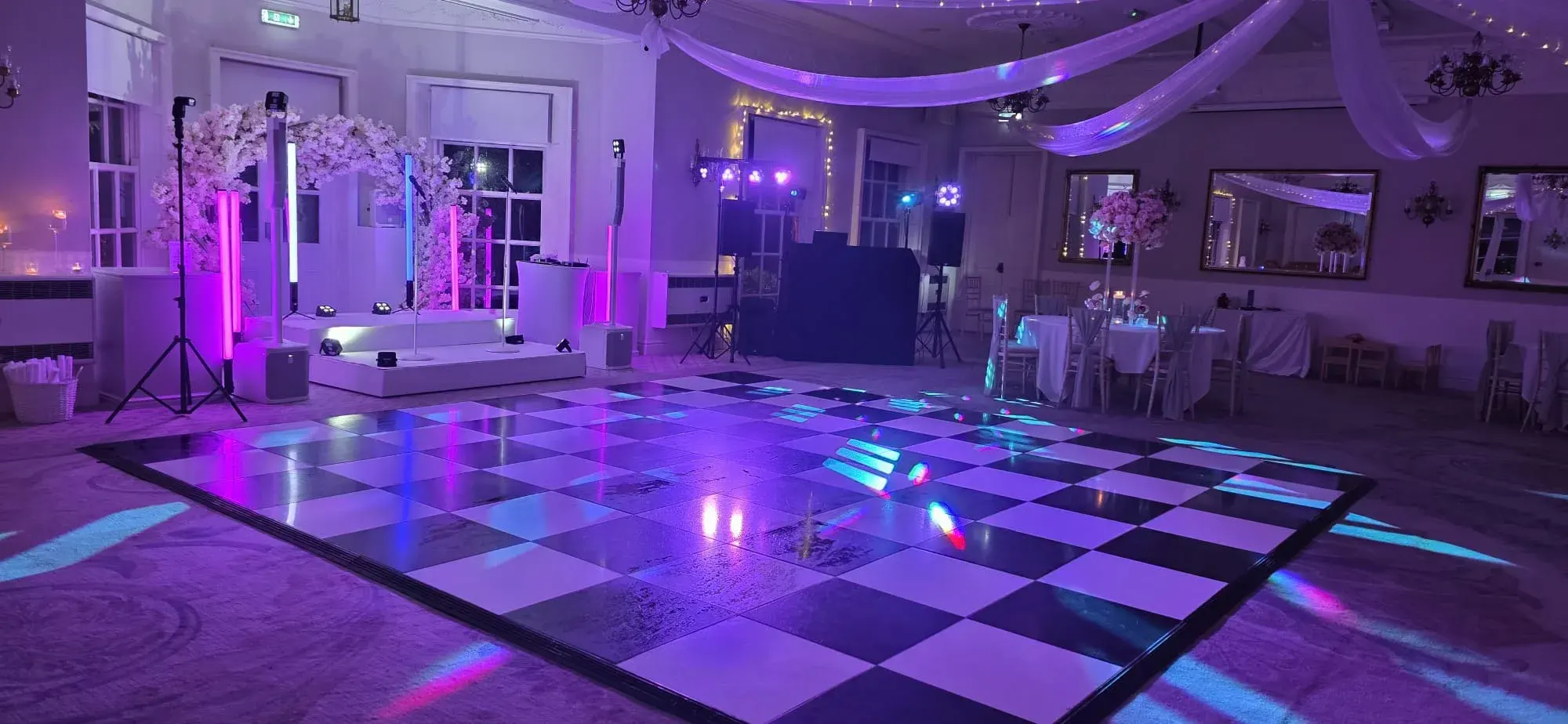 Black and white dance floor with a DJ booth, floral arch and purple lighting