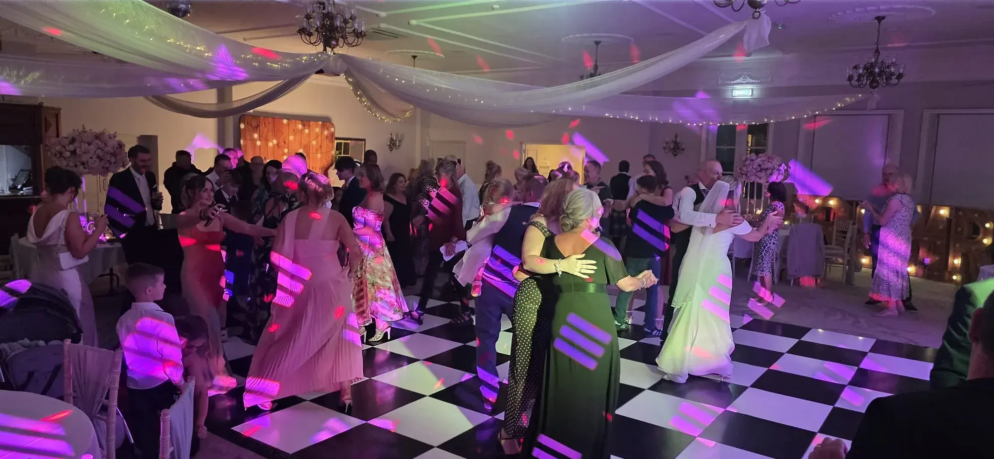 Wedding guests dancing together under pink and purple disco lights
